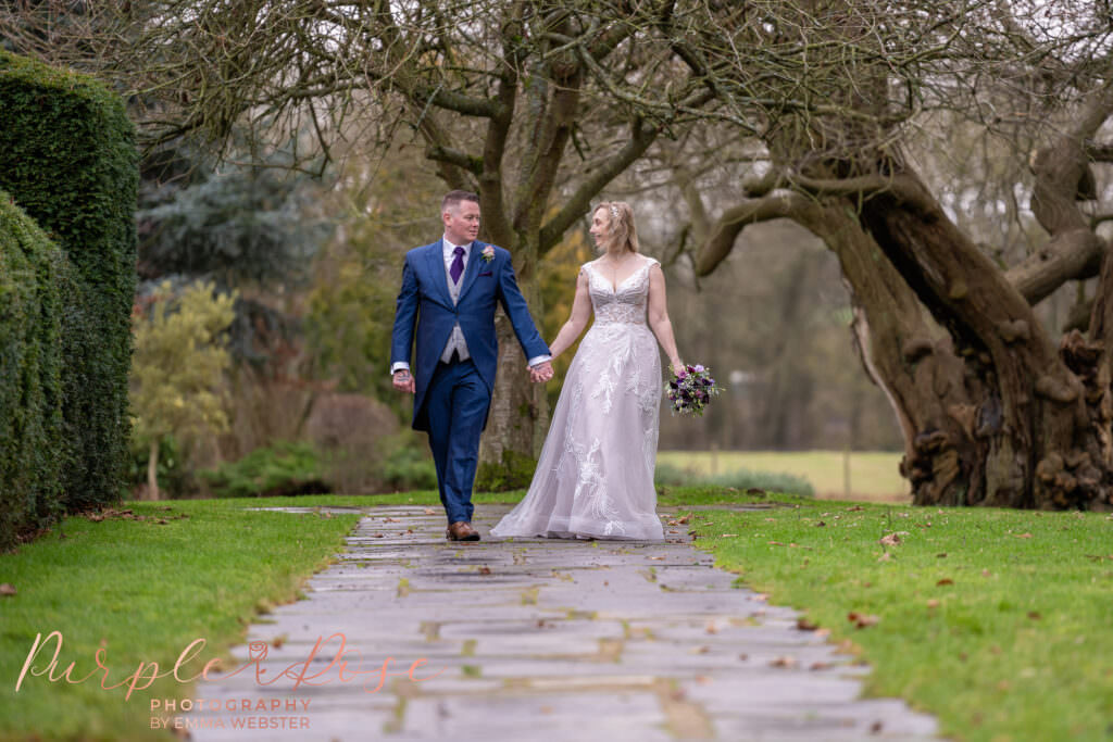 Bride and groom wlaking hand in hand along a cobbled pathway