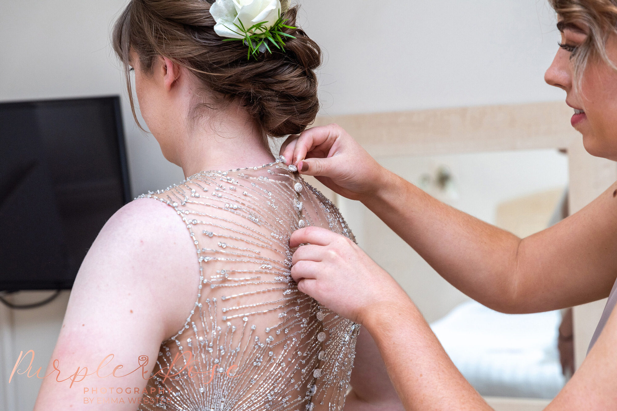 Bridesmaid buttoning up brides dress