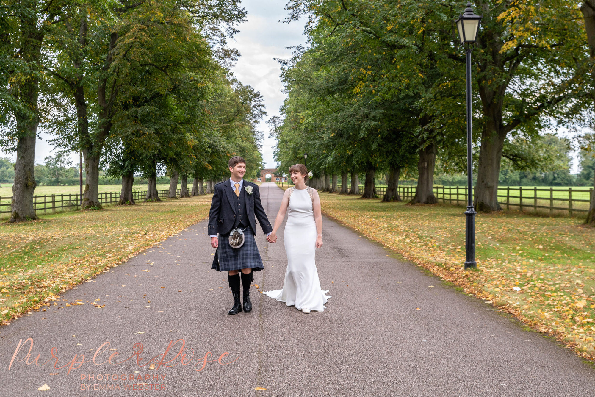 Bride and groom walking along tree lined driveway