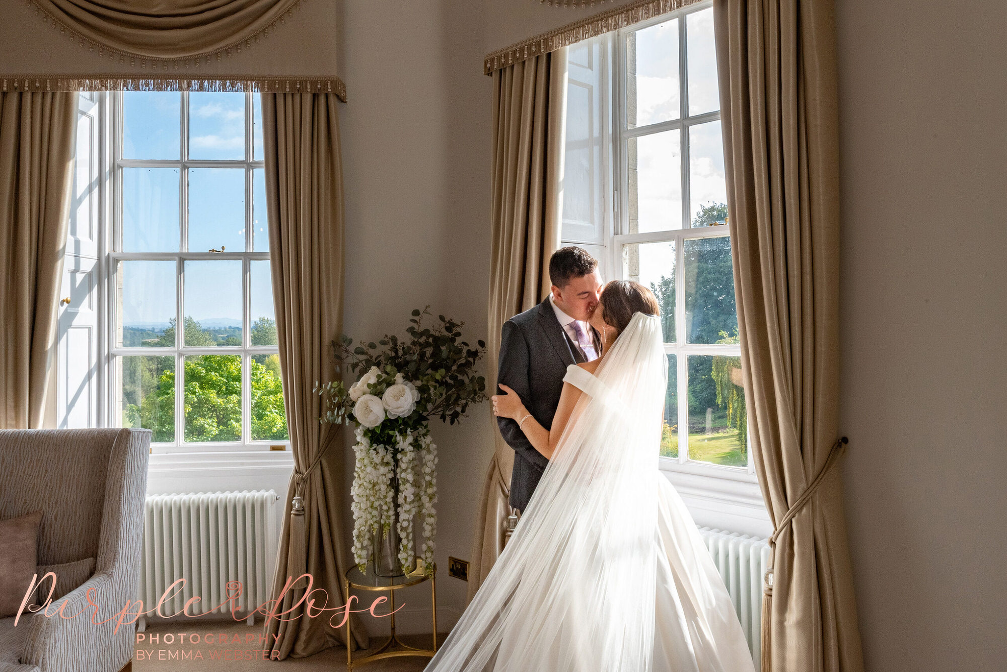 Bride and groom kissing in front of a window