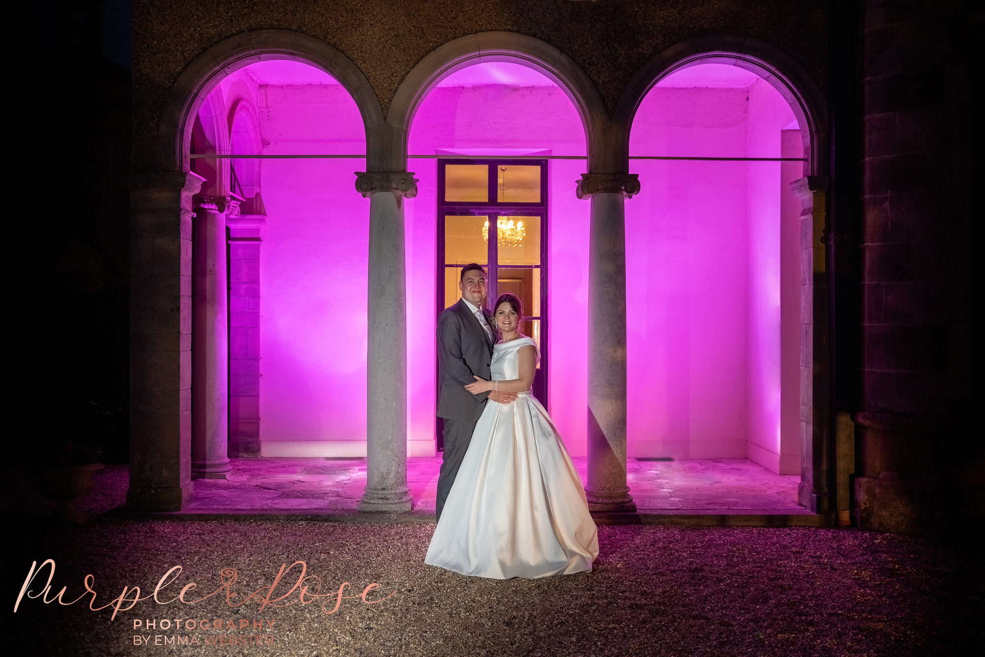 Night time wedding photo under pink lit arches 