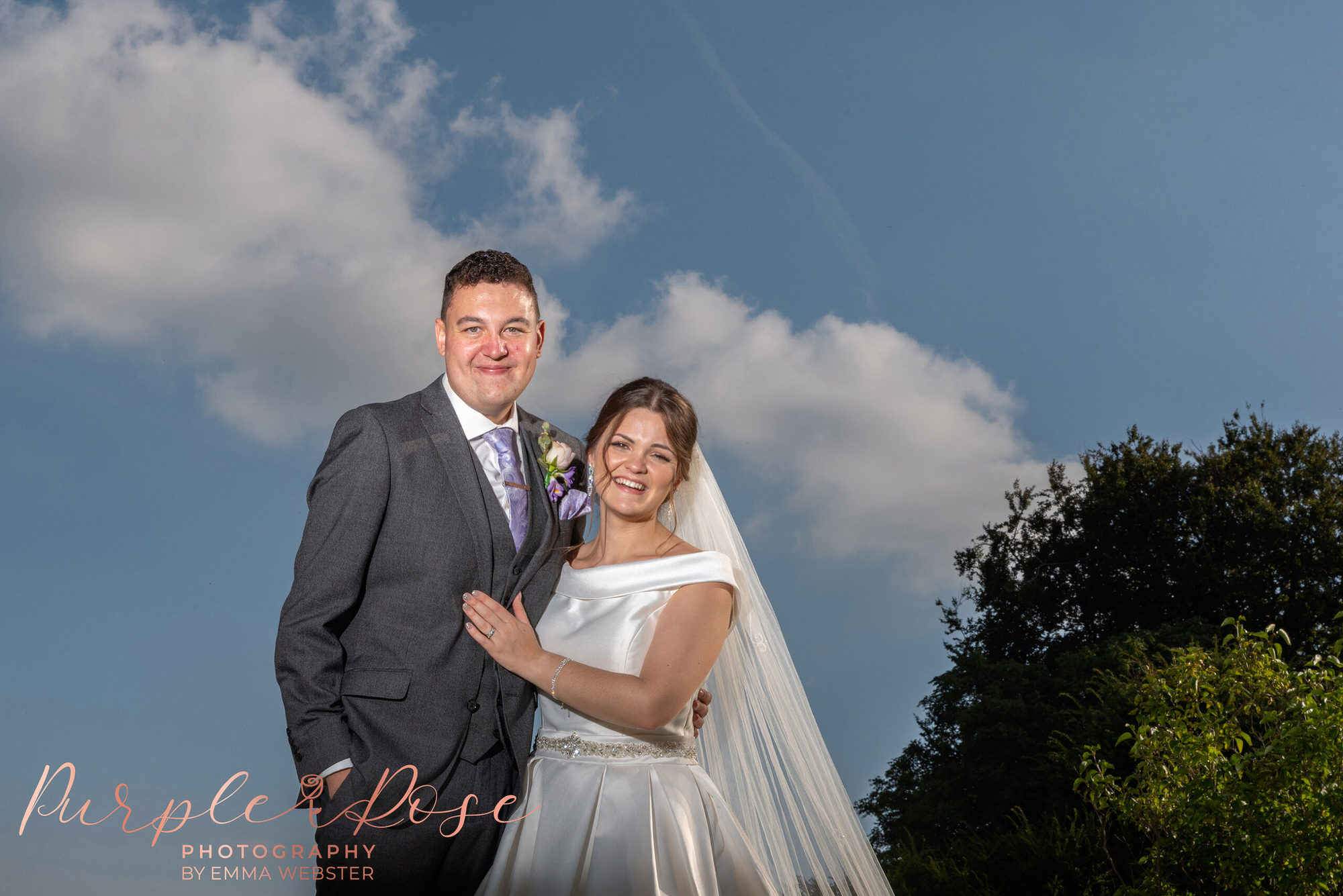 Bride and groom smiling in front of blue sky