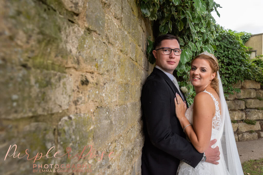 Bride and groom embracing by a brick wall