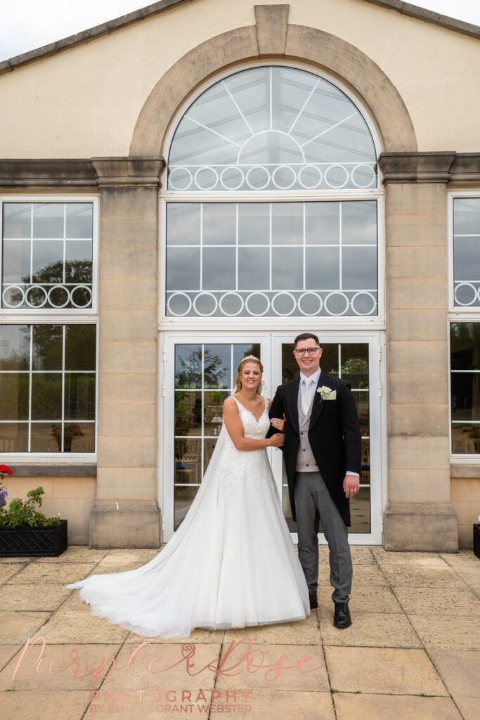Bride and groom stood arm in arm in front of an orangery