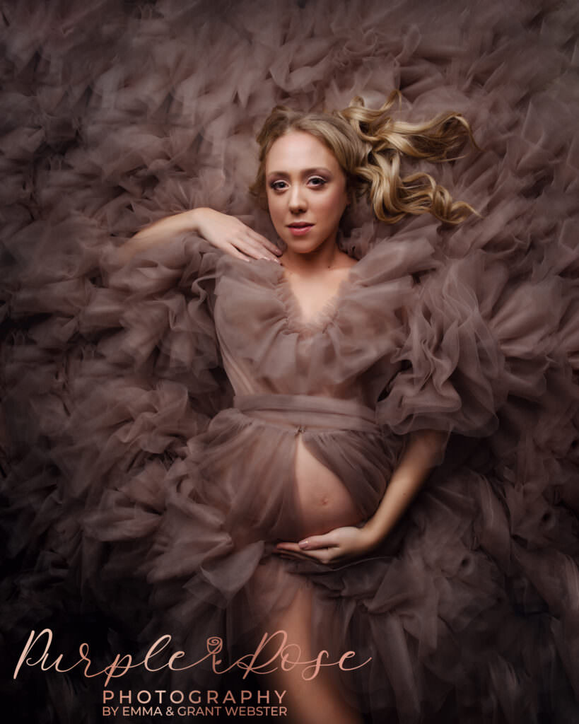 Mum to be laying on the floor surrounded by pink ruffles at photoshoot in Milton Keynes