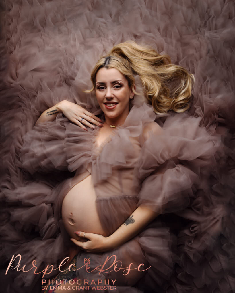 Mother laying down surrounded by ruffles of fabric during her maternity photoshoot in Milton Keynes
