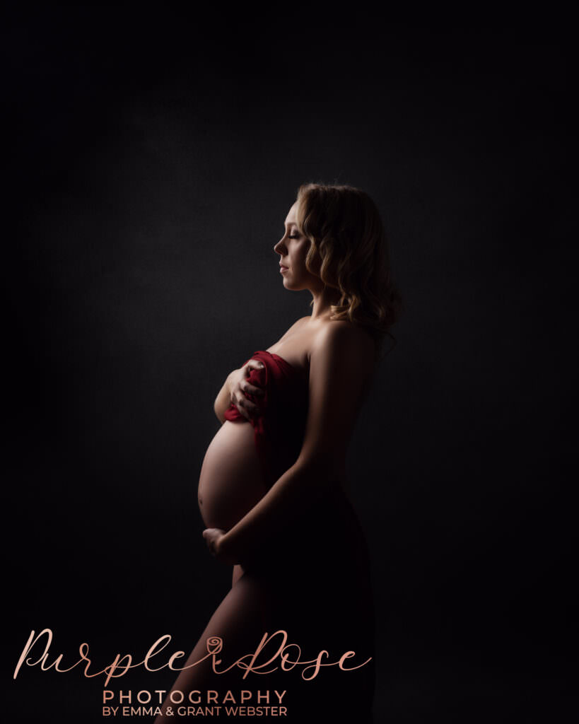Pregnant woman draped in fabric side lit at her studio photo shoot in Milton Keynes