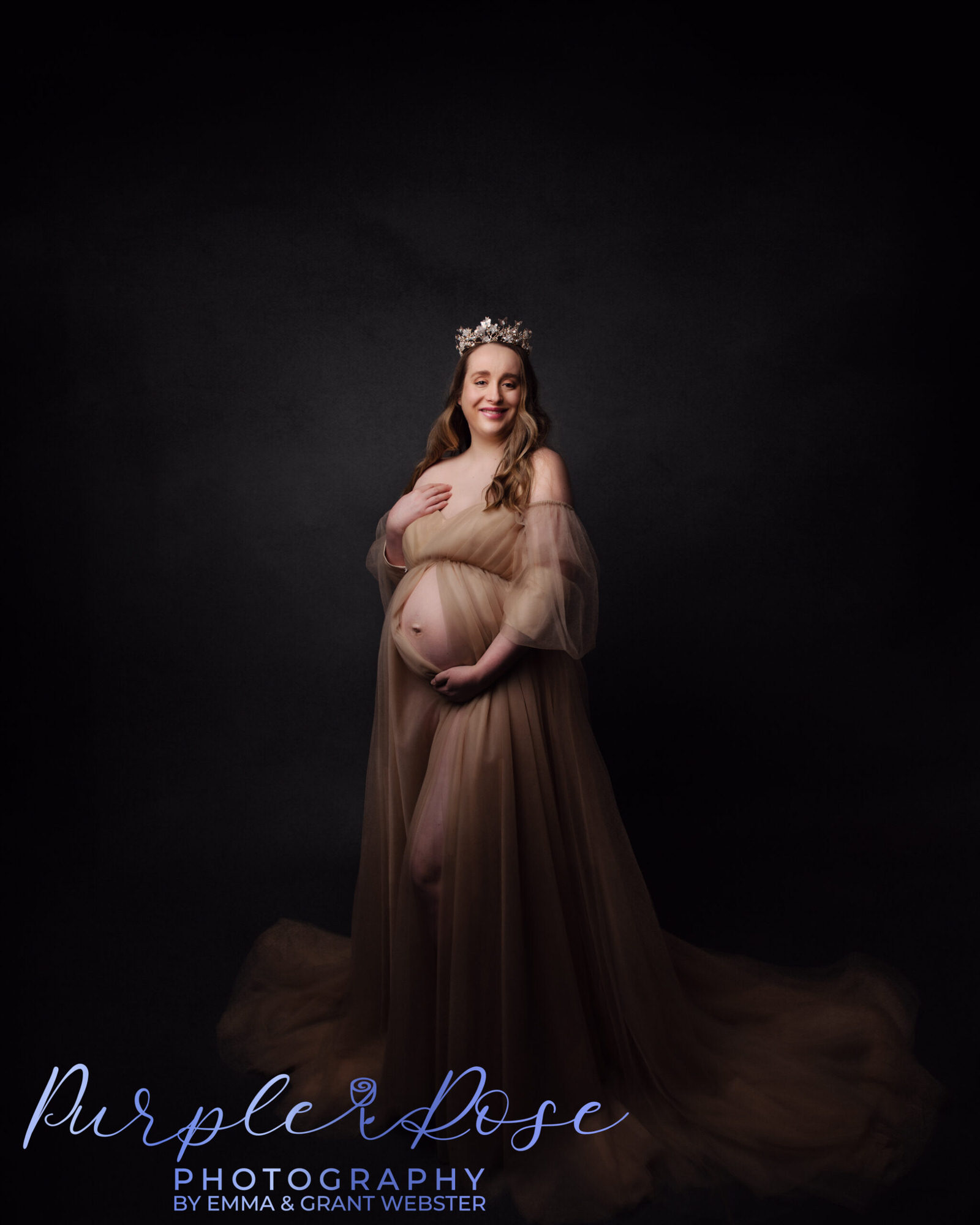 Pregnancy photo of a lady in cream tulle dress and crown cradling her baby bump at her maternity photoshoot in Milton Keynes