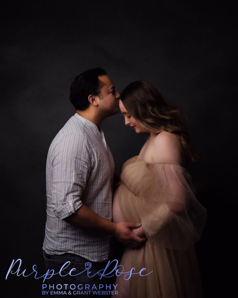 Husband kissing his wife on the forehead during maternity photoshoot in Milton Keynes