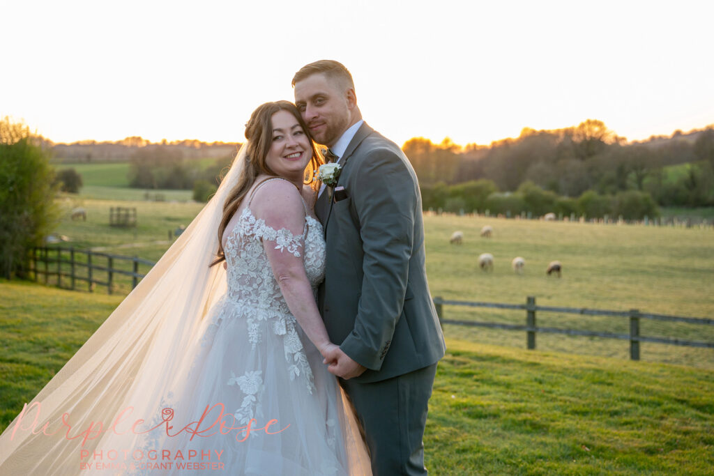 Bride and groom holding hands on their wedding day in Milton Keynes, stood outside with fields behind them.