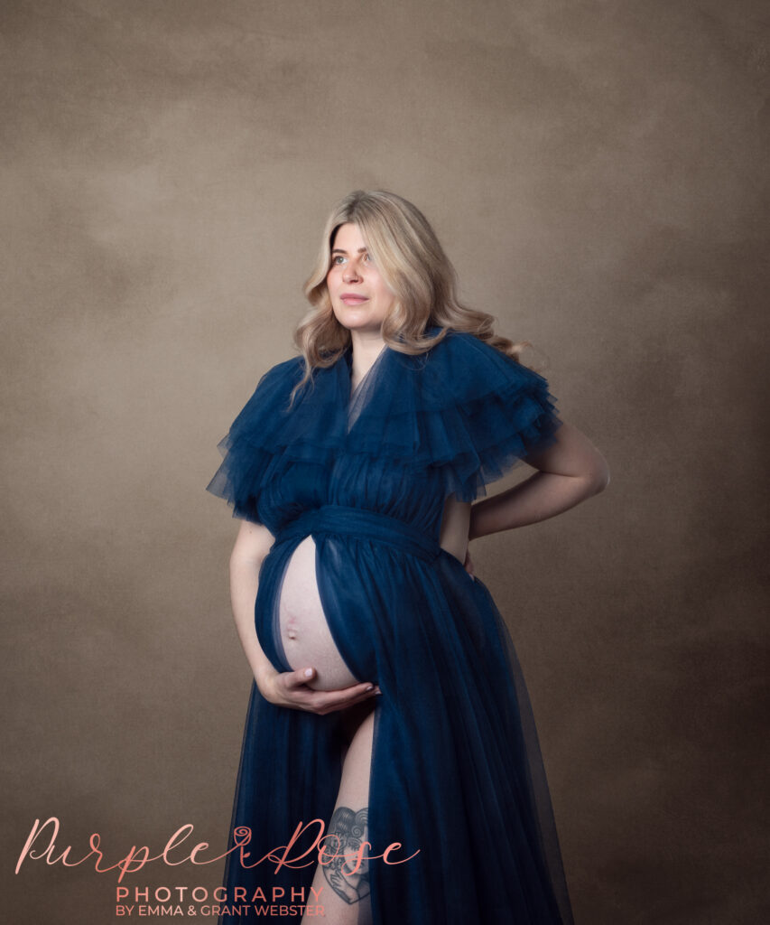 Photo of mum to be in a blue gown, cradling her baby bump at her maternity photoshoot on Milton Keynes