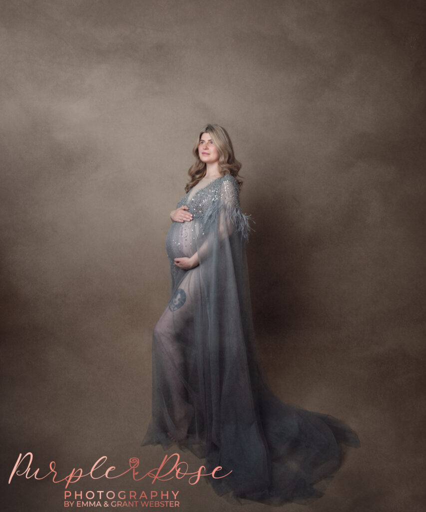 Photo of mum to be at her maternity photoshoot cradling her baby bump in a grey sequin tulle gown