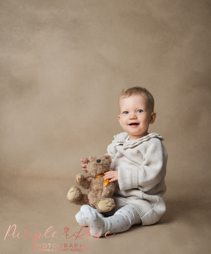 phot of a baby holding a teddy smiling at the camera at her 1st birthday photo shoot in Milton Keynes