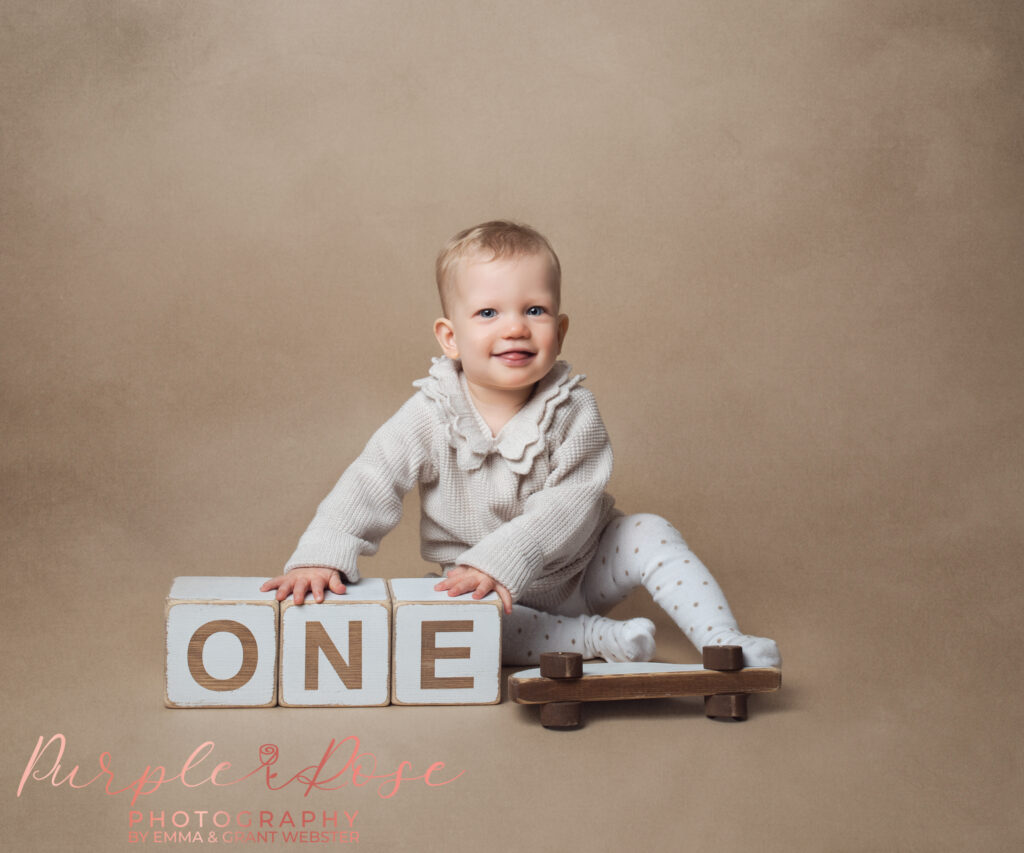 Photo of smiling baby leaning on wooden blocks at her 1st birthday photoshoot on Milton Keynes