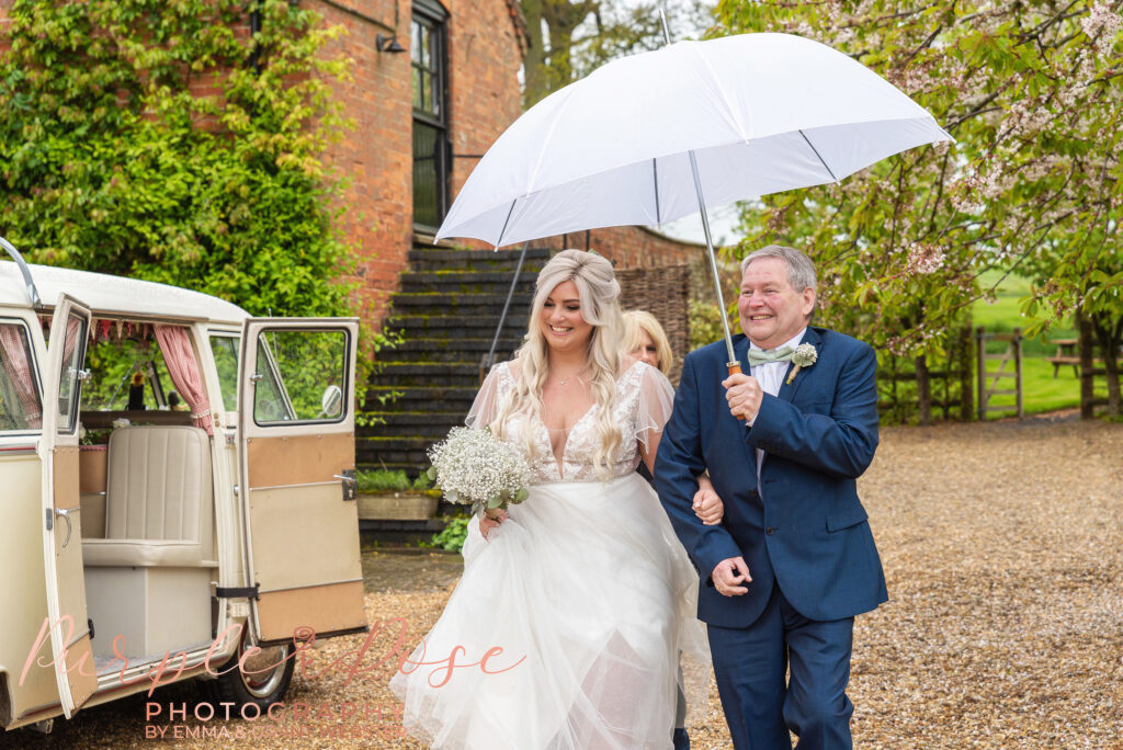 Photo of bride shelttering under an umbrella as she arrives at her wedding venue in Northampton