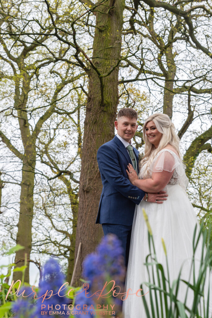Photo of bride and groom stood in front of blue flowers on their wedding day in Northampton