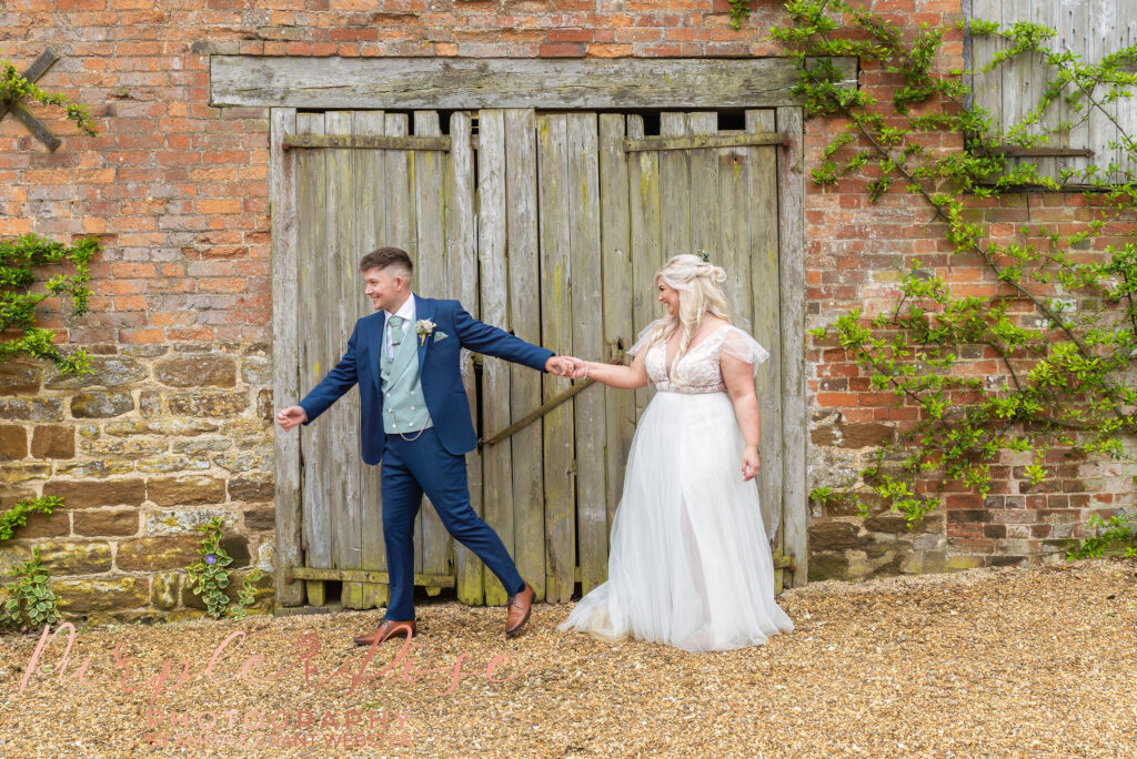 Bride and groom laughing in fornt of a barn door on their wedding day in Northampton