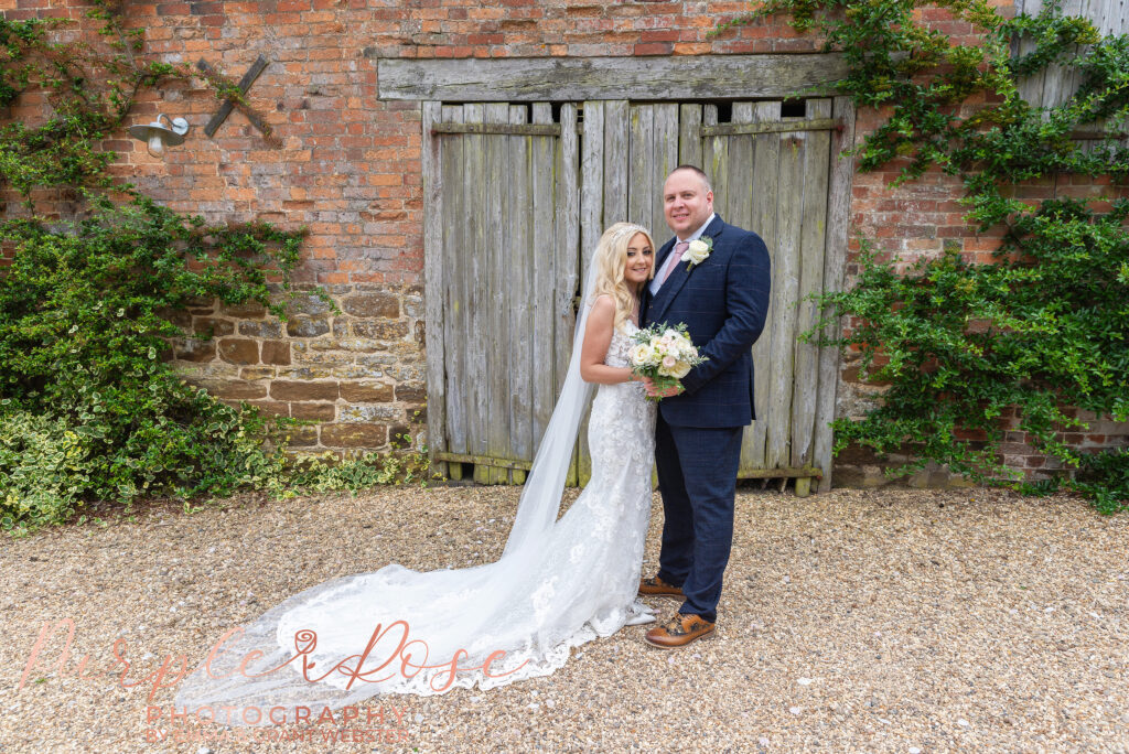 Photo of bride and groom stood by a barn door on ther wedding day in Northampton