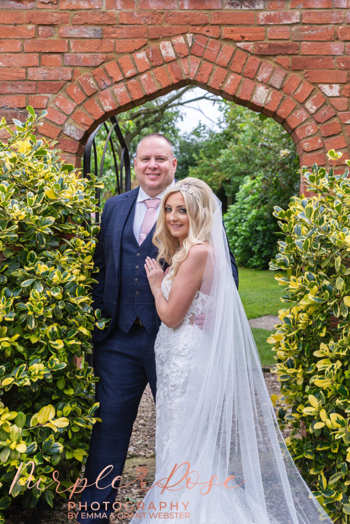 Photo of bride and groom stood in front of a brick gate on their wedding day in Northampton