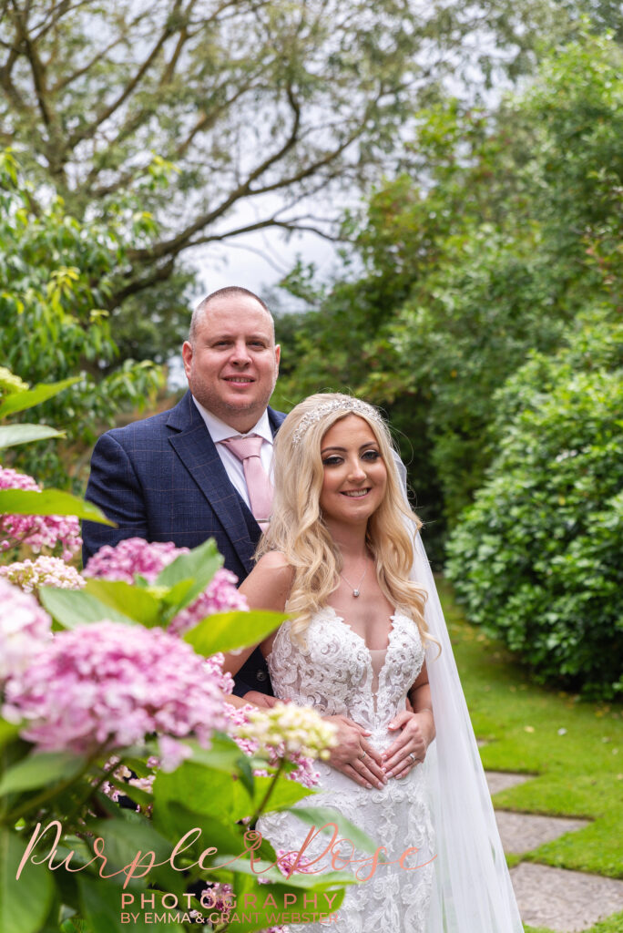 Photo of bride and groom stood in fornt of flowers in a garden on their wedding day in Northampton