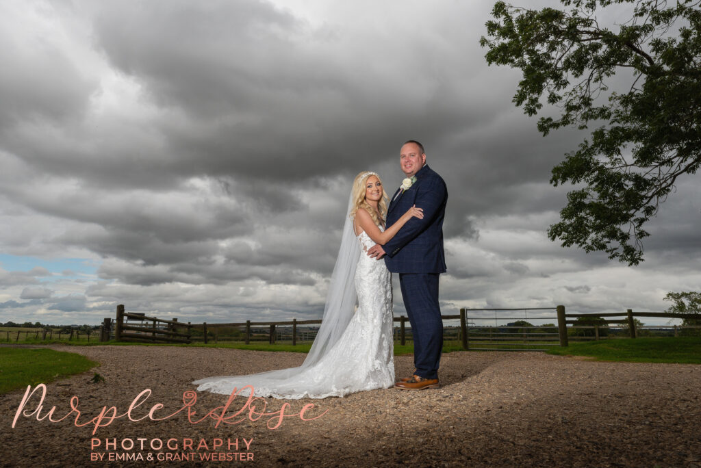 Photo of bride and groom stood in fornt of a stormy sky on their wedding day.