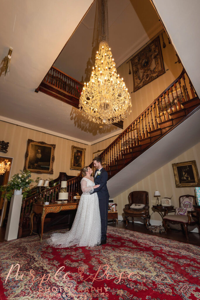 Photo fo a bride and groom on their wedding day stood under a chandalier on their wedding day in Milton Keynes