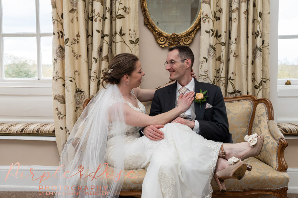 Photo of bride and groom sat together laughing on a formal chair on their wedding day in Milton Keynes