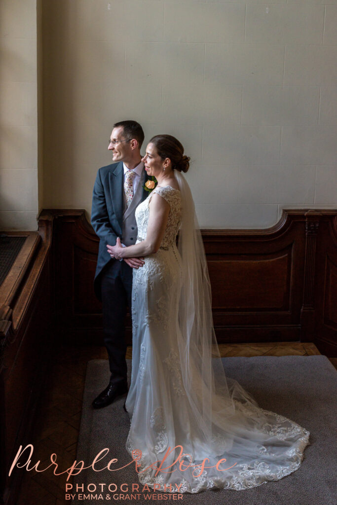 Photo of bride and groom stood arm in arm looking out a window on their wedding day in Milton Keynes